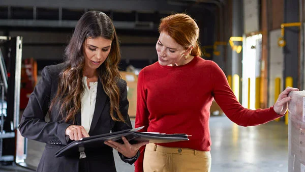 A Old Dominion sales person and customer use a handheld tablet around prepared freight pallets, coordinating loading and shipping activities.